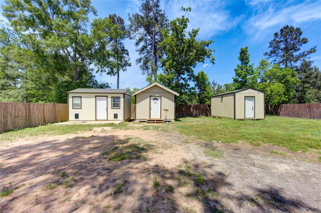 Spacious backyard featuring three storage sheds, surrounded by a wooden fence and mature trees, offering ample storage and privacy.
