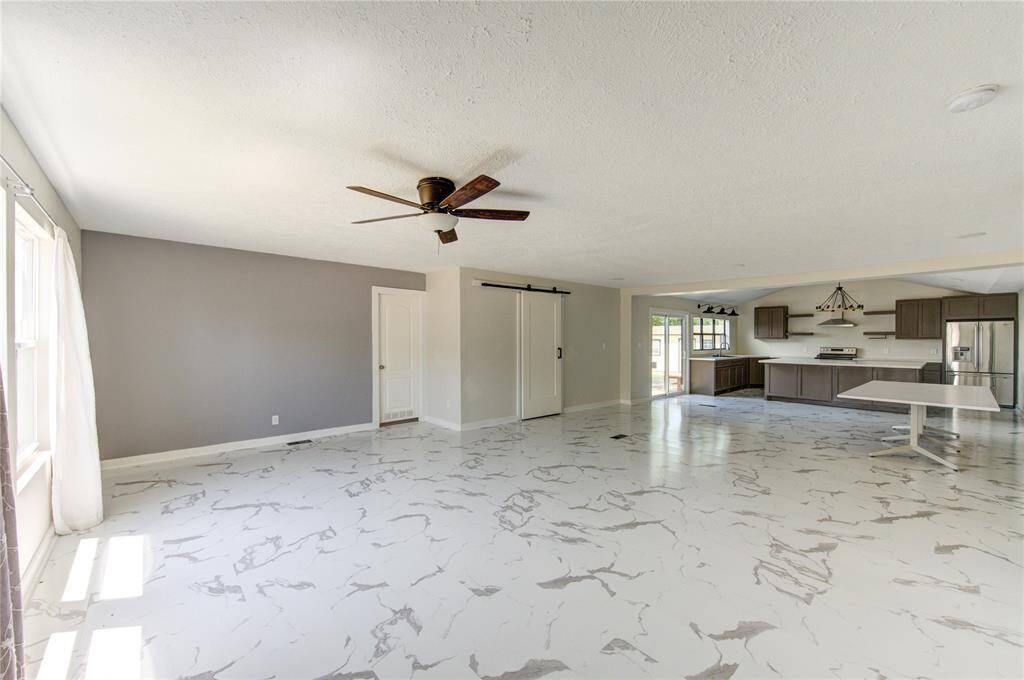 This spacious open-concept living area features modern marble-look flooring, a ceiling fan, and abundant natural light. The kitchen includes sleek cabinetry, stainless steel appliances, and a large island, perfect for entertaining.