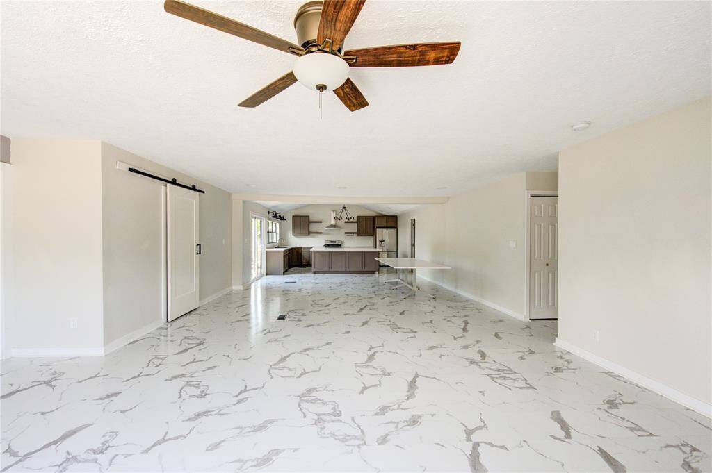 Bright open-concept living space with modern marble-patterned flooring, ceiling fan, and a stylish kitchen featuring a sliding barn door and stainless steel appliances.
