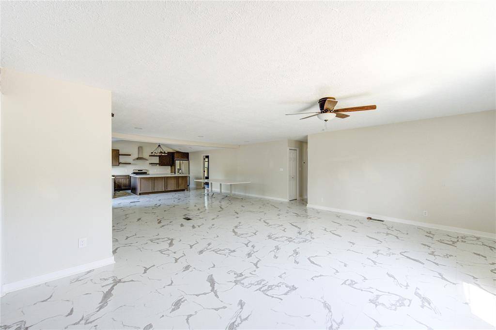 Spacious open-concept living area with modern marble-like flooring, neutral walls, a ceiling fan, and a view into the kitchen featuring wooden cabinets and stainless steel appliances.