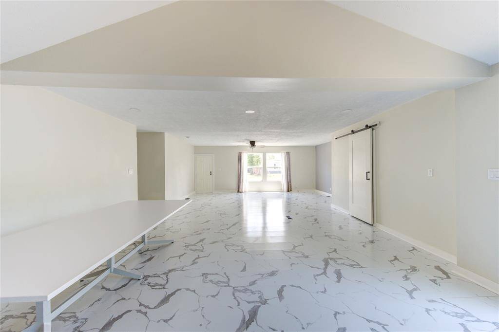 This spacious room features a bright, open layout with modern marble-style flooring and neutral walls. It includes a large window for natural light and a sliding barn door for a contemporary touch.