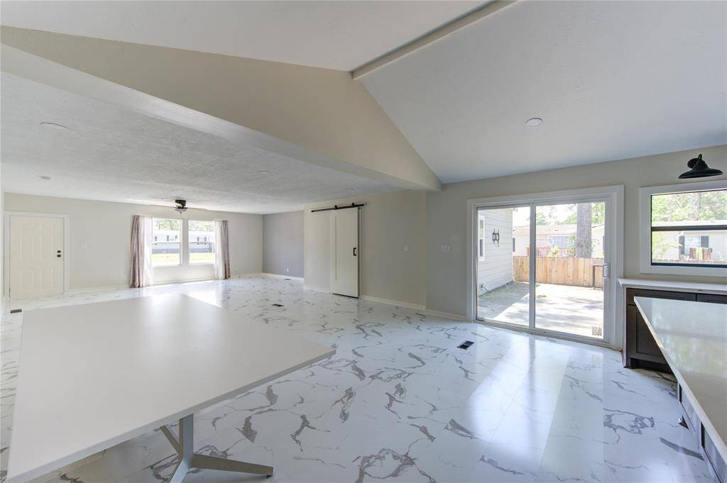 This spacious, open-plan living area features modern marble-patterned flooring, abundant natural light from large windows and sliding glass doors, and a sleek barn door. Ideal for entertaining, it seamlessly connects to an outdoor space.