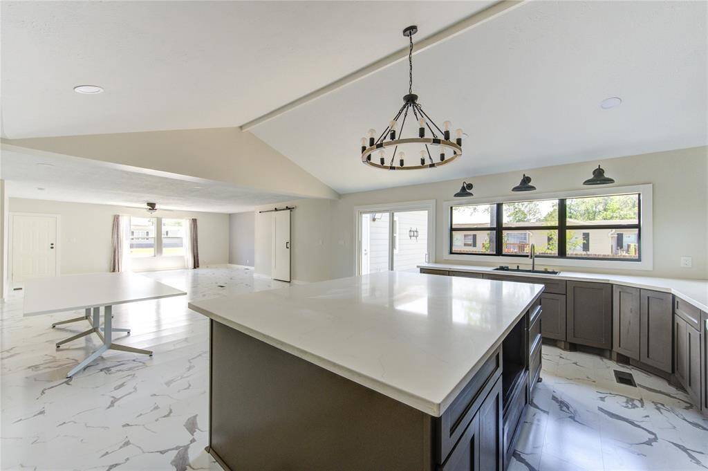 This spacious, open-concept kitchen and dining area features modern design with a large island, marble-like flooring, and ample natural light from large windows. The elegant chandelier and sleek cabinetry add a touch of sophistication. Perfect for entertaining and family gatherings.