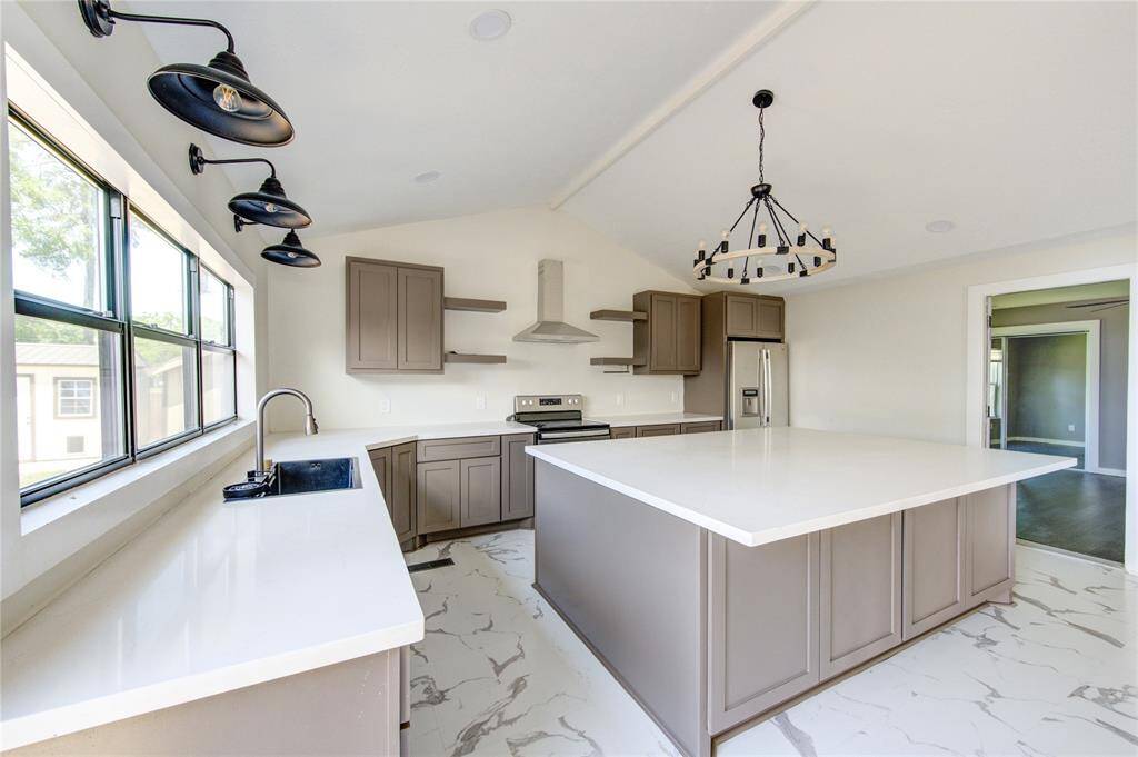 This modern kitchen features a spacious layout with a large island, sleek countertops, and elegant cabinetry. It includes stainless steel appliances, ample natural light from large windows, and stylish lighting fixtures, offering a perfect blend of functionality and contemporary design.