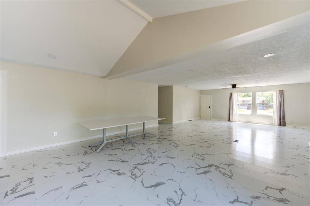 Spacious living area with high ceilings and large windows, featuring modern marble-patterned flooring. The room is bright and open, offering plenty of natural light and a versatile layout.