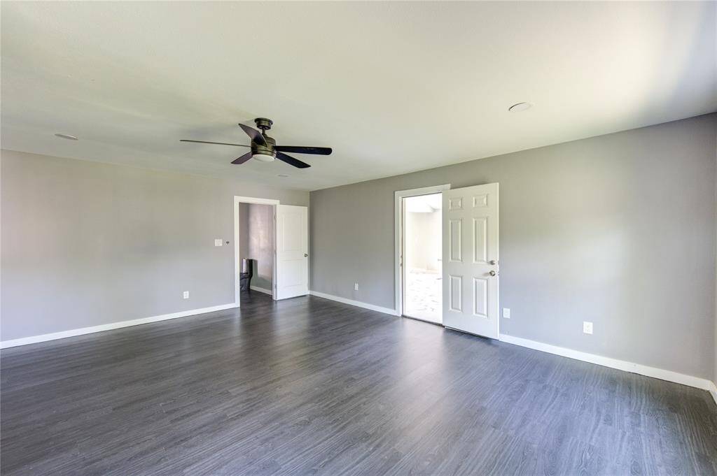 This spacious room features modern gray flooring, neutral walls, a ceiling fan, and ample natural light from a window. It includes a door leading to another area, providing versatility for use as a living or multipurpose space.
