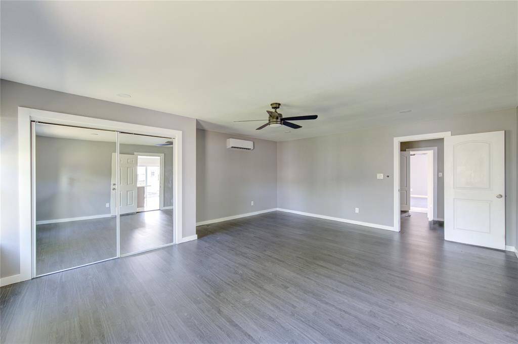 This spacious room features modern gray flooring, neutral walls, a ceiling fan, mirrored closet doors, and ample natural light, creating a bright and airy atmosphere.