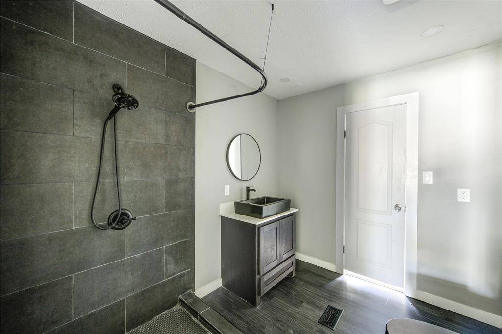This bathroom features a modern design with dark tile shower walls, a sleek black showerhead, and a stylish vanity with a black vessel sink. The room is well-lit with a minimalist aesthetic.