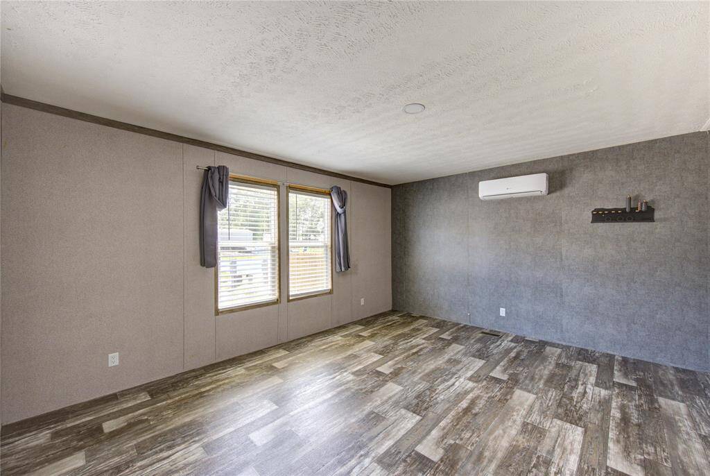 Spacious room with large windows, letting in natural light. Features modern wood-look flooring, neutral walls, and a wall-mounted air conditioning unit for comfort. Ideal for customization.