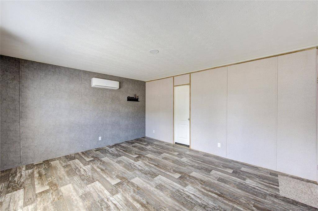 This room features a modern, minimalist design with neutral walls and wood-look flooring. It includes a wall-mounted air conditioning unit for comfort.