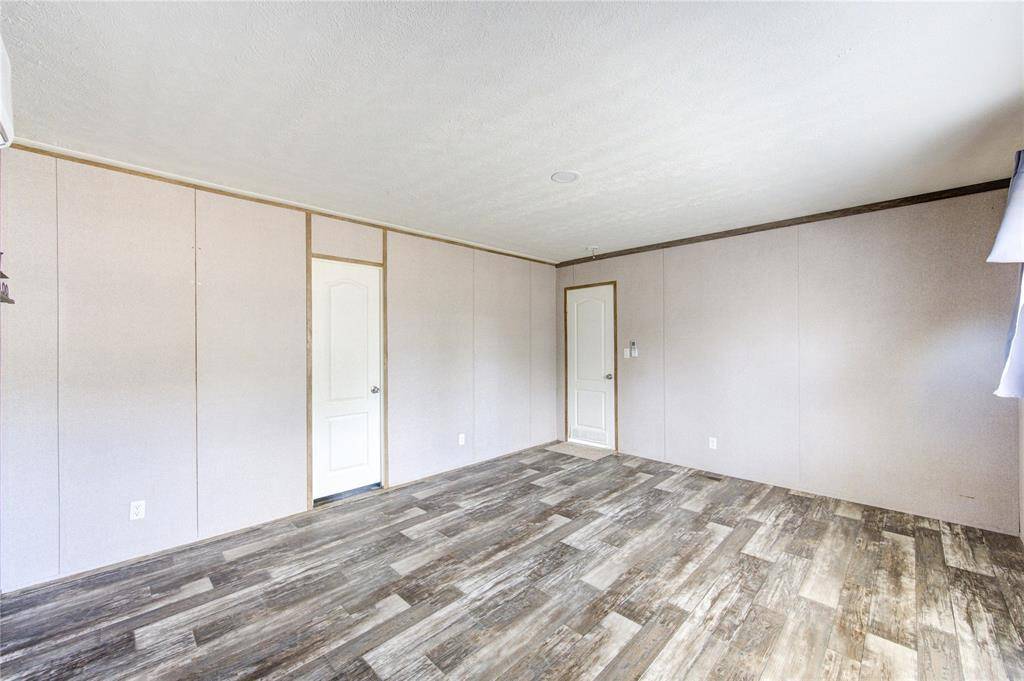 This spacious room features neutral-colored walls and wood-style flooring, providing a versatile and modern look. It has two doors and ample natural light, ideal for customization.