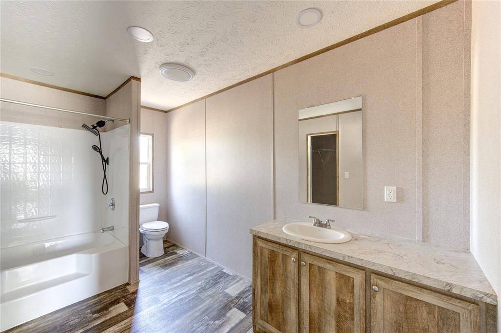 Bright and spacious bathroom featuring a bathtub with shower, modern fixtures, a large vanity with a mirror, and stylish wood-look vinyl flooring.