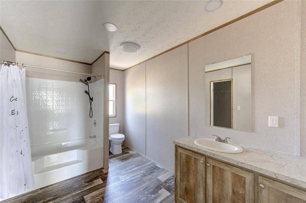 This bathroom features a clean, modern design with a spacious layout. It includes a bathtub with a shower, a single-sink vanity with a marble countertop, a large mirror, and a window for natural light. The flooring has a wood-like finish for a warm touch.