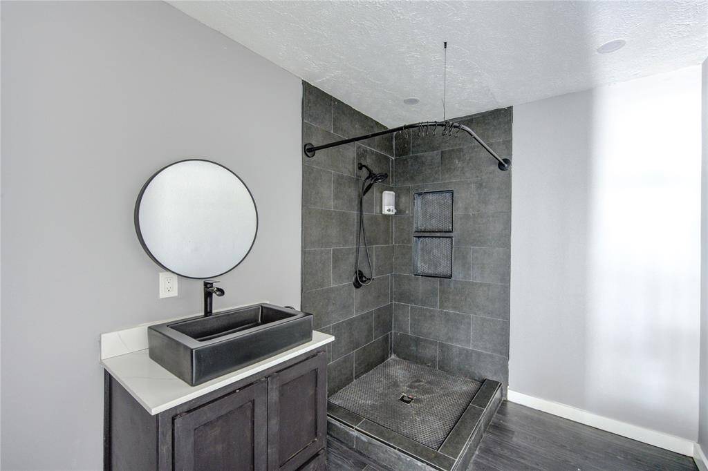 Modern bathroom with a sleek, dark-tiled shower featuring a rainfall showerhead. The vanity has a rectangular black sink and a round mirror, creating a stylish, contemporary look.