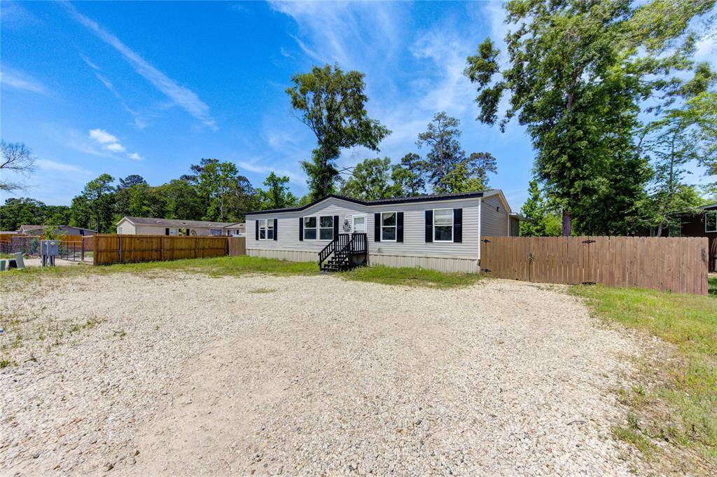 This property features a spacious manufactured home with a large gravel driveway and fenced yard, surrounded by trees for added privacy.