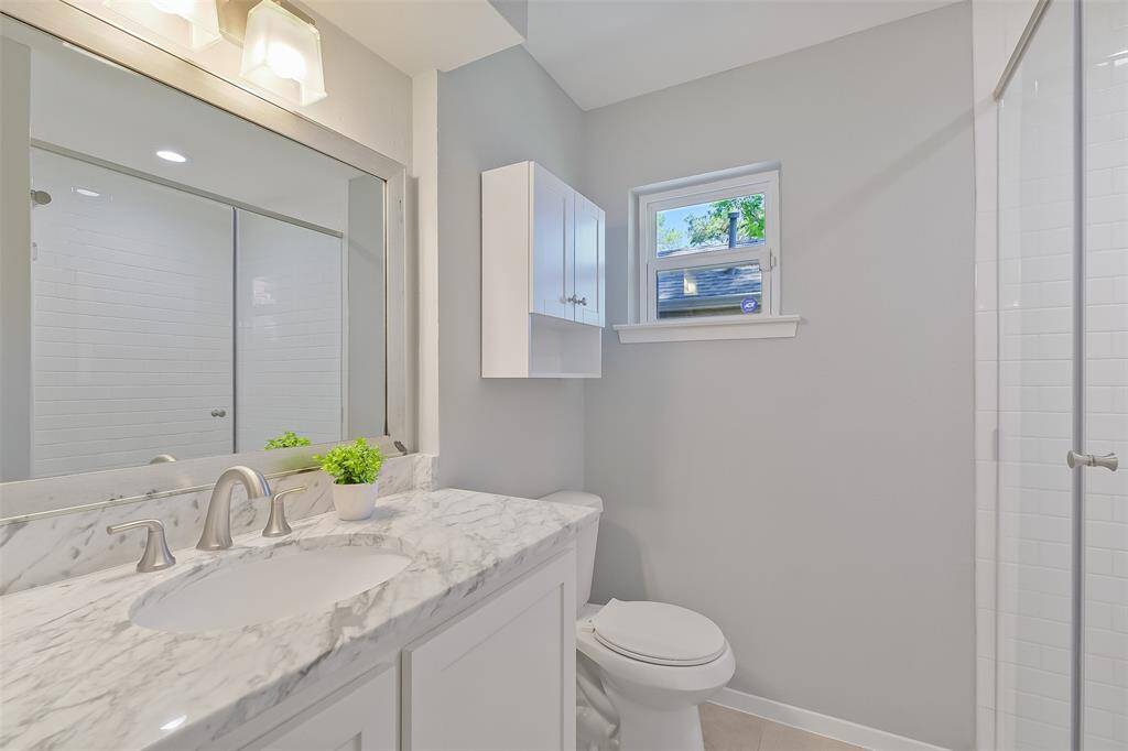 Luxurious primary bathroom featuring a vanity with an elegant carrera marble countertop and custom cabinetry. The expanded shower with a glass door offers a modern touch, while additional shelving and a built-in hamper provide extra storage and convenience.