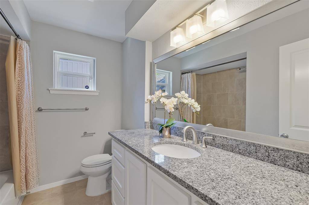 Beautiful guest bathroom with a large vanity offering ample storage and a granite countertop. A large decorative mirror and vanity lights enhance the space, while the tub/shower combination adds functionality. Additional storage, including a built-in hamper, is conveniently located just outside the bathroom.