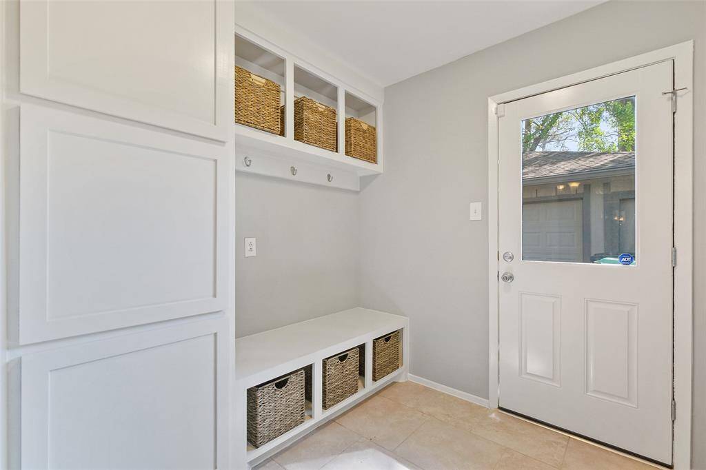 Functional utility room/mud room located just off the breakfast room, with easy access to the backyard and garage. Features include tile floor, washer/dryer connections, and a mudroom area with built-in cabinets, storage bins, and a bench for convenience. Hooks for hanging bags and coats add to the practicality of this well-organized space.