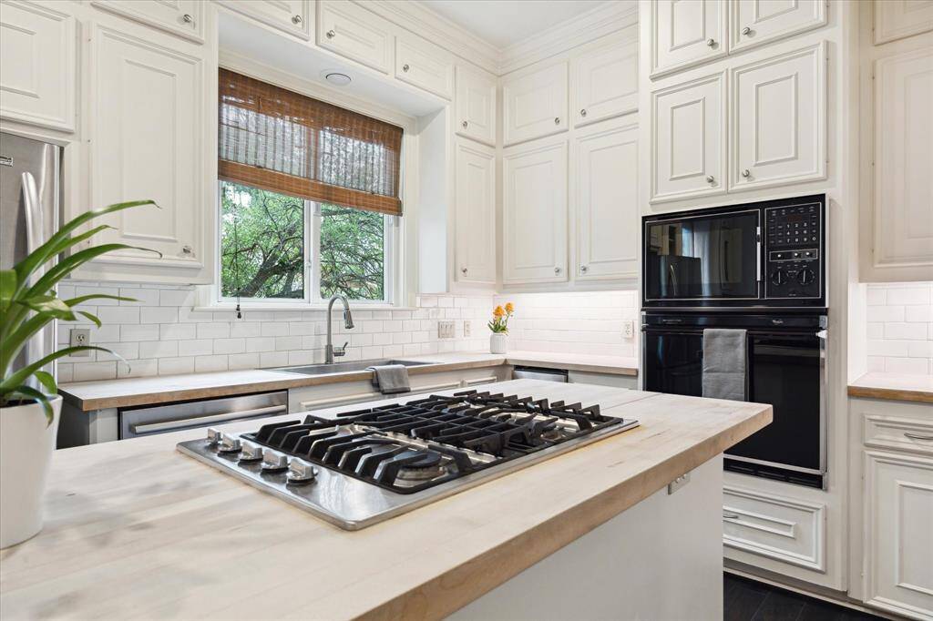 This kitchen is bright and inviting, featuring a large casement window above the sink, gas cooktop on a central island, and subway tile backsplash.