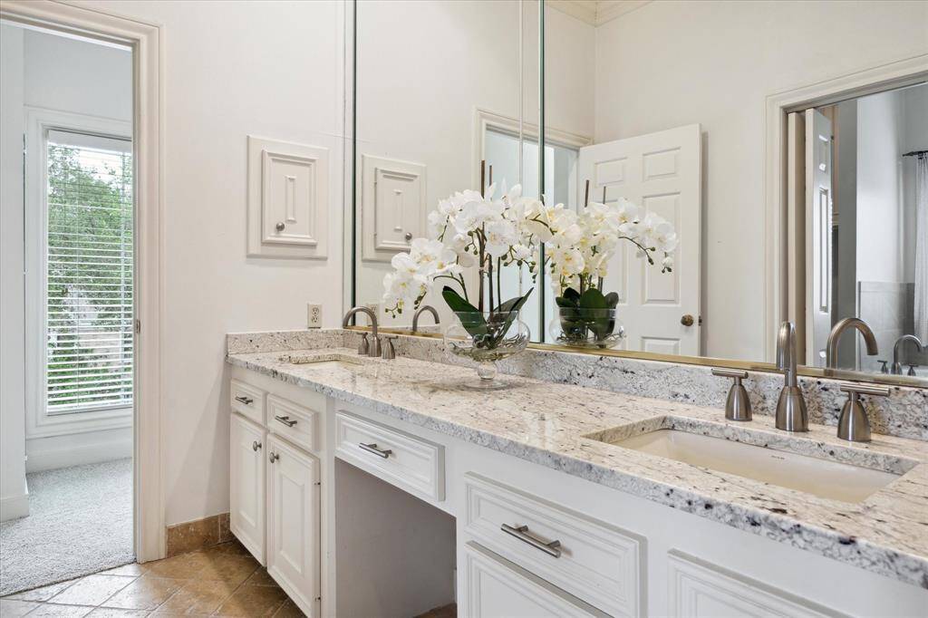 Bright and elegant Primary Bathroom featuring double sinks and a vanity with granite countertops, stylish faucets, and large mirrors. Natural light pours in through a windows, enhancing the fresh, modern feel.