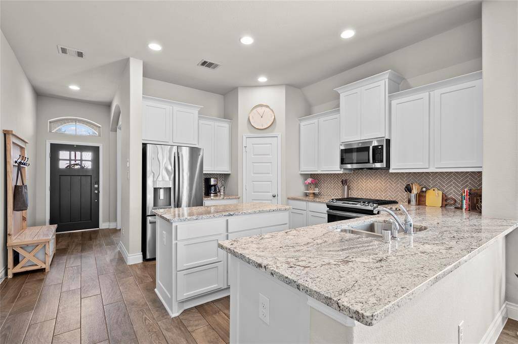 Entertain in style in this beautiful kitchen featuring granite countertops, white painted cabinets, a herringbone tile backsplash, and a large island!