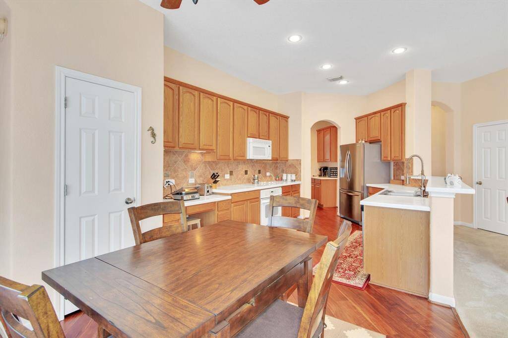This kitchen features warm wooden cabinets, a white corian countertops, and modern appliances. The space is well-lit with recessed lighting, combining functionality with a cozy atmosphere.