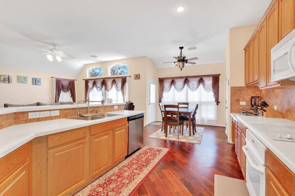 A bright, open kitchen with warm wood cabinetry and a breakfast nook. It features hardwood floors, large windows with elegant drapes, and modern appliances, providing a cozy and inviting space for dining and cooking.
