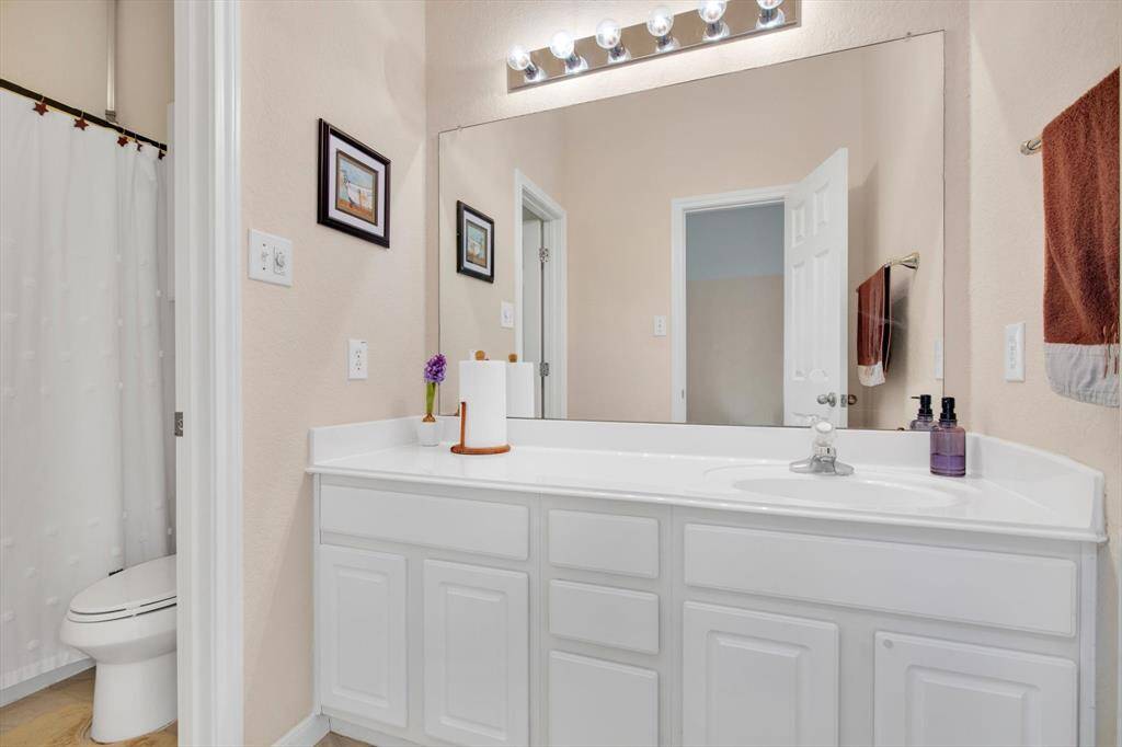 This bathroom features a spacious vanity with ample storage, a large mirror with stylish lighting, and a clean design with neutral tones.