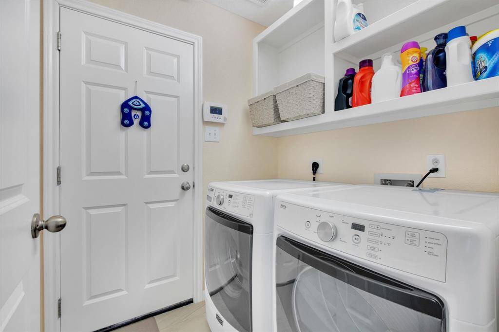 Laundry room featuring modern appliances, ample shelving for storage, and a convenient door leading outside.