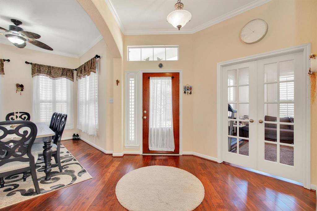 Bright and welcoming entryway with hardwood floors, featuring a front door with side windows. Adjacent is a dining area with a ceiling fan. French doors lead to home office room, adding charm and functionality.