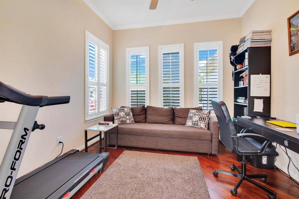 Home Office features has hardwood floors, abundant natural light from tall windows with shutters, and built-in shelving for organization.