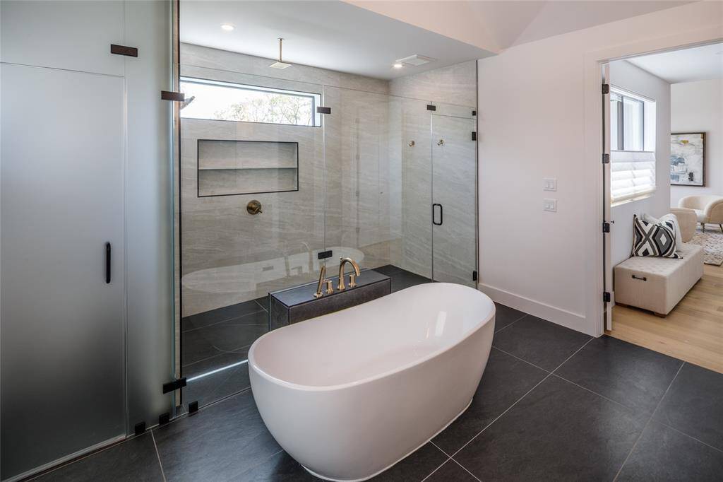 An elevated primary bathroom to a spa-like environment. Oversized walk-in shower with seamless glass door. Slipping into a soaking tub with warm water after a rough day is almost like magic
