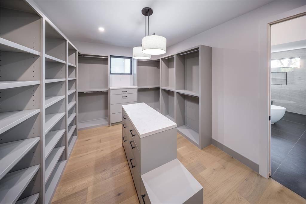 HERS private dressing room with center island, custom built-in drawers and shelves and an elegant hanging chandelier