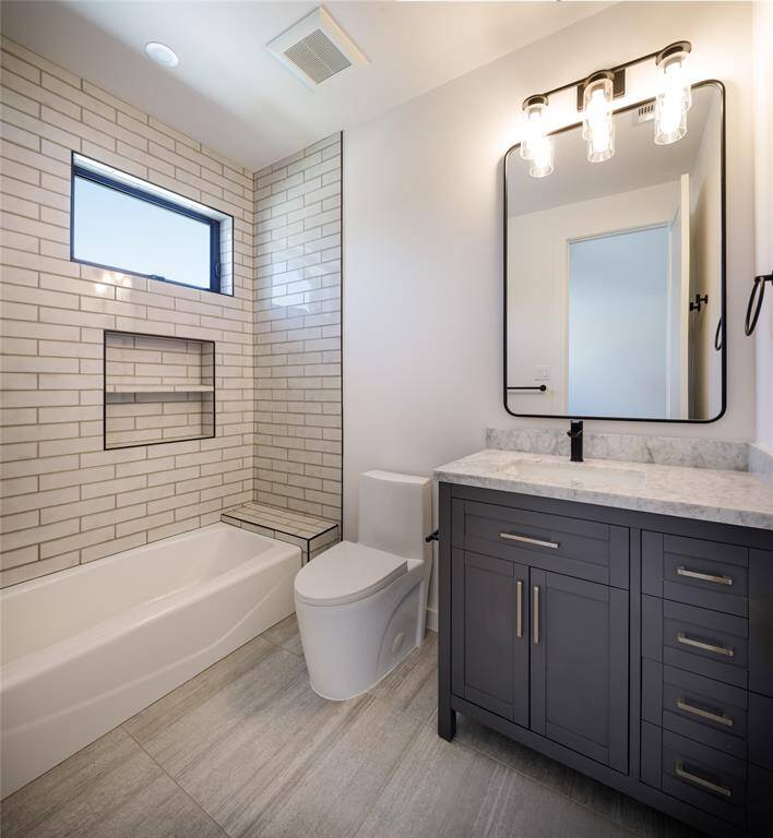 En-suite bathroom with tub/shower, furniture style built-in vanity and sconces over a framed mirror