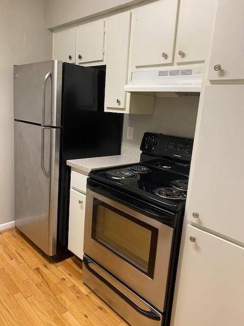 This is an old picture before the tenant moved in. This kitchen has stainless steel appliances, including a refrigerator and stove. It features white cabinetry and laminate flooring, offering a clean and functional space.