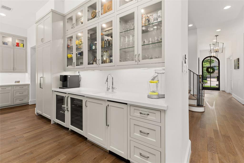 Wet bar w/ sink, wine fridge, ice maker w/ wood paneled front, glass shelving & glass front cabinets w/ lighting, under cabinet lighting.