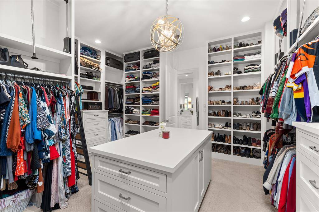 Expansive custom closet with built-ins, center island, plenty of lighting & upper storage solutions.