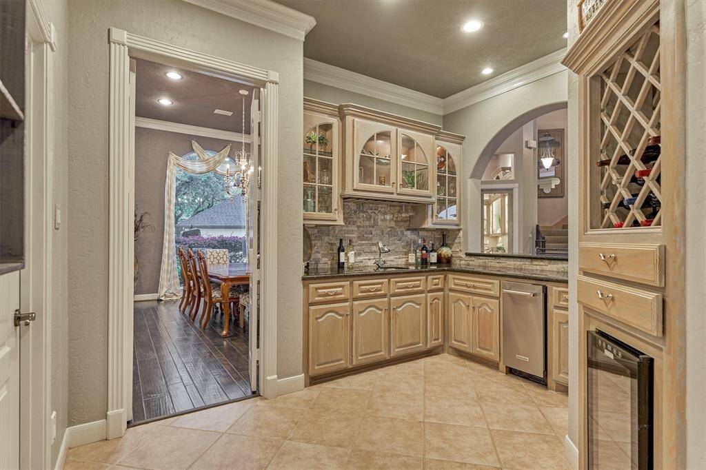 Perfect for entertaining, the wet bar located just off the formal dining room and entry foyer features wine storage, a wine refrigerator, ice maker, sink, and custom cabinetry—offering a stylish and functional space for hosting guests with ease.