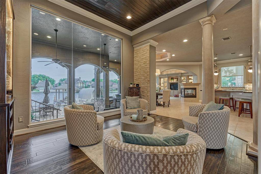 At the heart of the home, a beautiful sitting room offers an elegant setting to gather with family or friends. Framed by classic Doric-style columns, crown molding, and stone accents, the space is enhanced by a warm wood plank ceiling. A large picture window captures unobstructed views of the pool and Lake Conroe, creating a serene and inviting atmosphere.