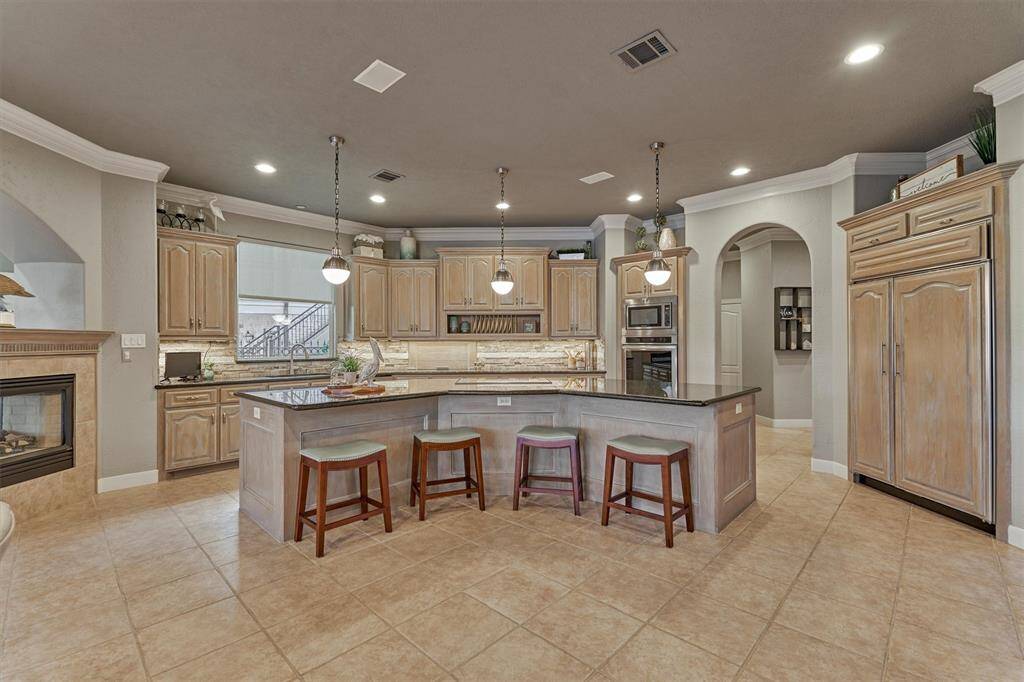 Another view of the kitchen highlights the expansive island and built-in refrigerator/freezer. The arched opening beyond leads to the laundry room, powder room, pantry, and garages—perfectly positioned for everyday convenience.