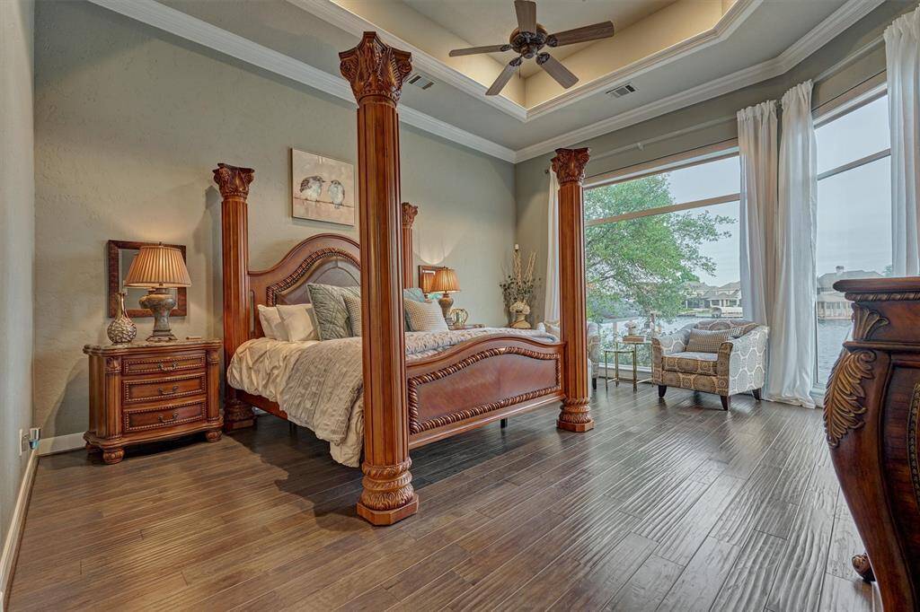 The first-floor primary suite exudes luxury with expansive windows framing stunning views of the lake and pool area. A tray ceiling with accent lighting and detailed crown molding adds a sophisticated, custom touch, creating a serene and elegant retreat.