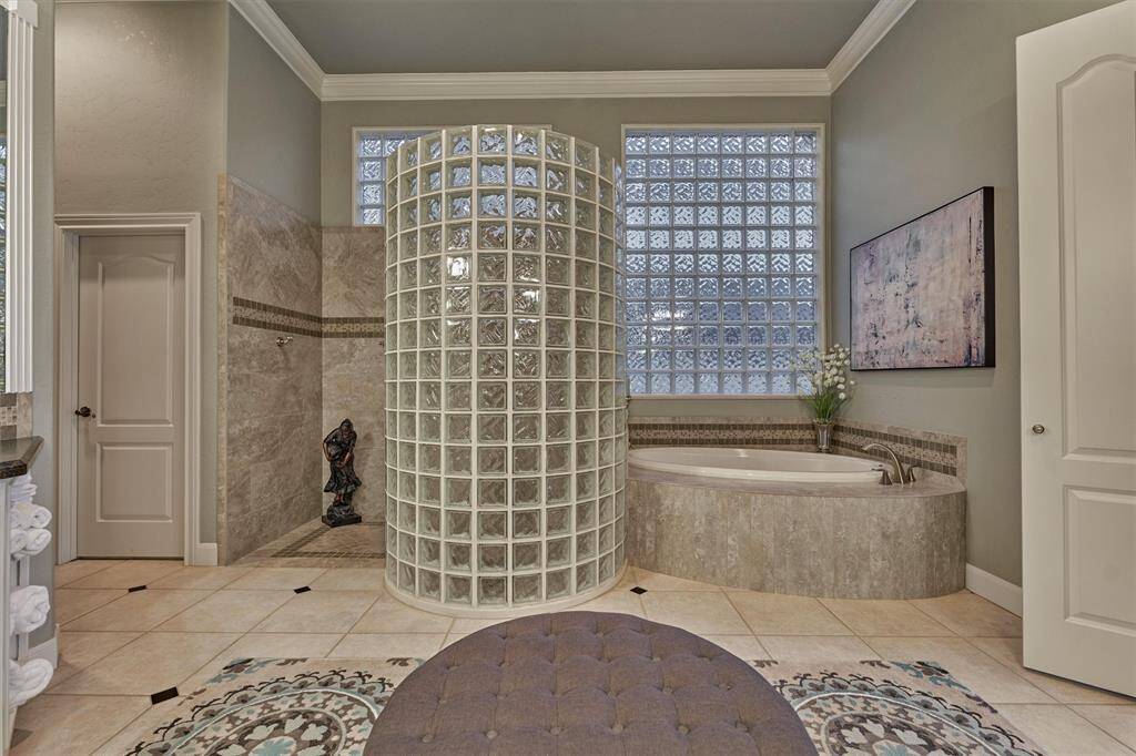 A view of the walk-in shower showcases its distinctive curved glass wall, paired beautifully with a corner soaking tub- creating a spa-like atmosphere with a touch of architectural flair.