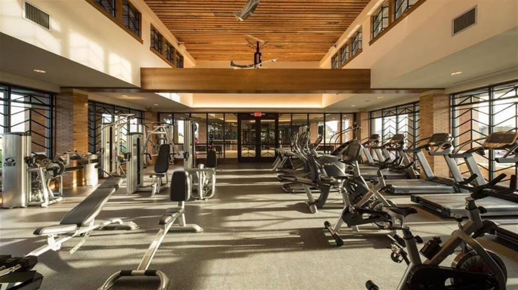 The fitness center features a diverse selection of cardio machines, Peloton bikes, free weights, resistance training machines, and various accessories like fitness balls and Pilates mats.