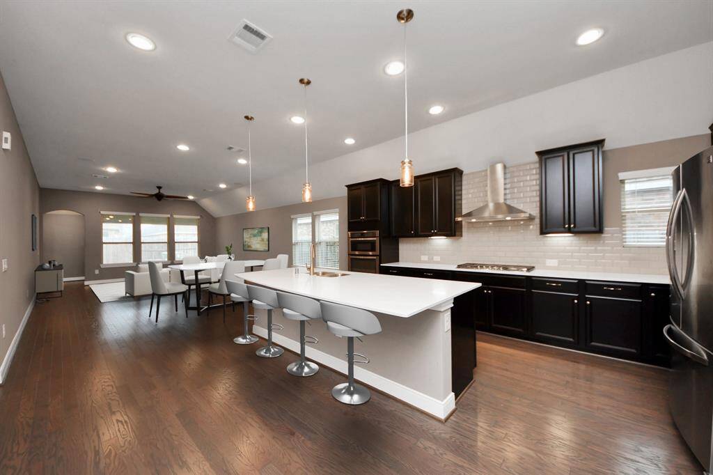 The kitchen is a chef’s dream, featuring a spacious island with elegant pendant lighting, sleek quartz countertops, a stylish subway tile backsplash, under-cabinet lighting, and stainless steel appliances.