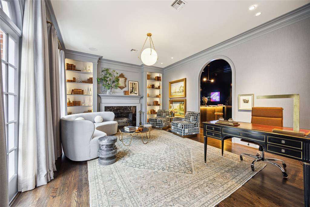 The sophisticated Living Room doubles as a stylish home office, featuring a gas fireplace with built-in shelving and an arched doorway leading to a moody, modern Entertainment Bar.