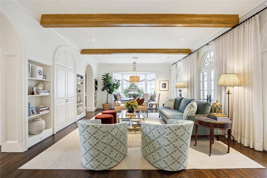 This inviting Family Room blends classic elegance with modern comfort, featuring exposed wooden beams, arched doorways, and abundant natural light streaming through a large bay window and several french doors