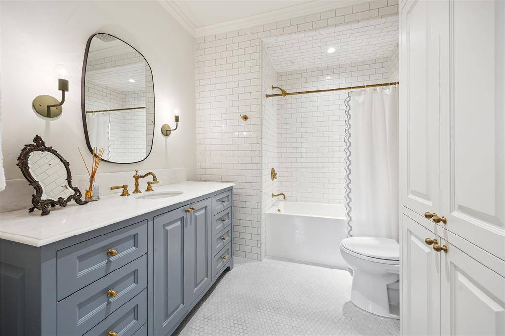 An elegant Bathroom showcases a soft blue vanity with gold hardware, a large sculptural mirror, and a shower-tub combo surrounded by timeless white subway tile.