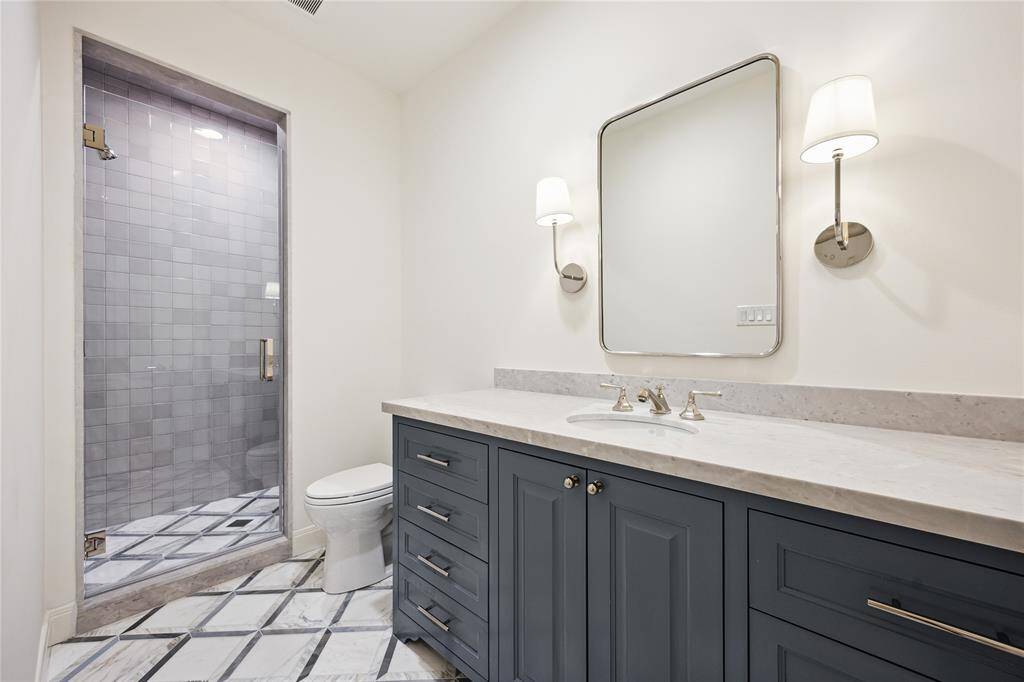 This elegant Third-Floor bathroom features a spacious walk-in shower, a sleek vanity with blue cabinetry, and chic marble flooring from Ann Sacks.