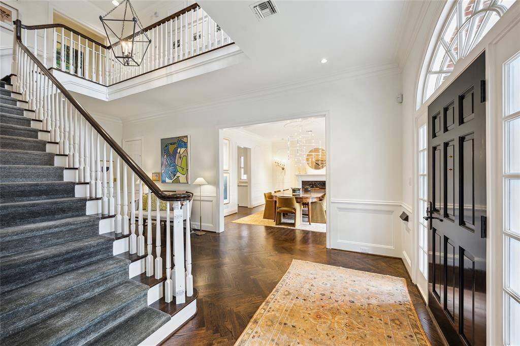 This sophisticated Entryway features a sweeping staircase with a custom Nepalese wool ombre runner, a striking black front door beneath a grand arched window, and an inviting view into a chic Dining Room