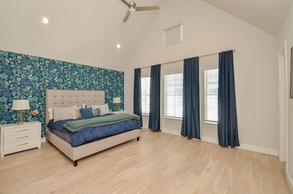 Custom accent wallpaper in primary bedroom adds appeal with the brushed gold drape rods and elegant blue paneled drapes accenting the high wall of windows.  The small window at top has a custom blind.